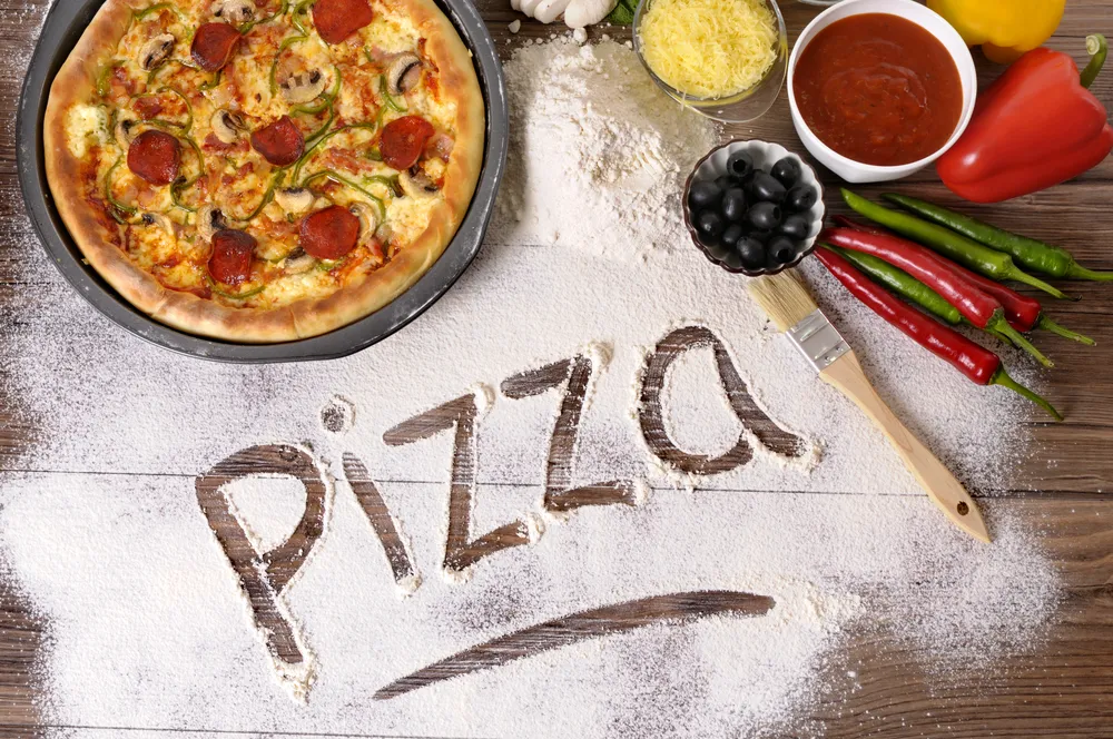 Pizza lista y pizza escrita sobre harina esparcida.